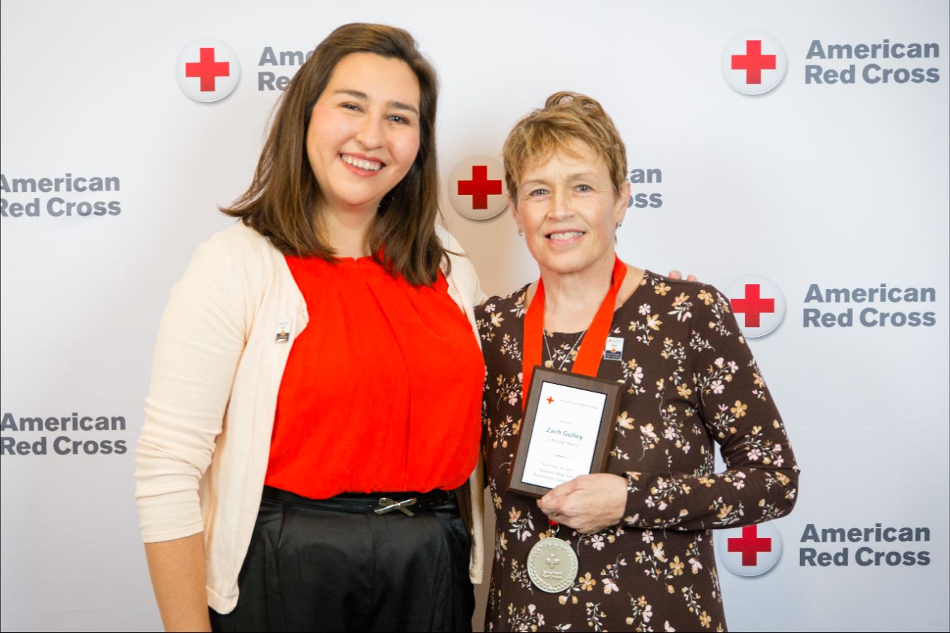 Two people posing for a picture, hugging each other with one holding an award