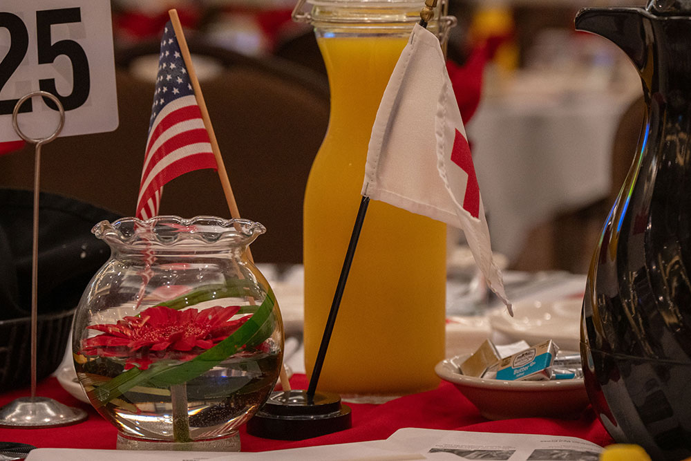dinner table with small american and red cross flags, glass of orange juice, and a flower in a glass jar at the Real Heroes Event.