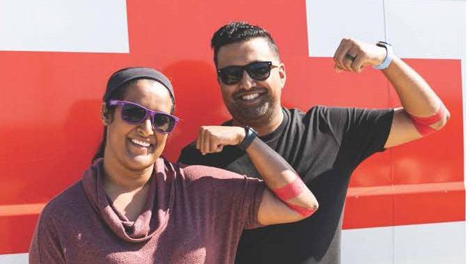 two people, with red bandages around their arm, flex their arms.