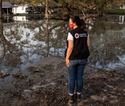 volunteer in red cross vest and mask looks at flooding