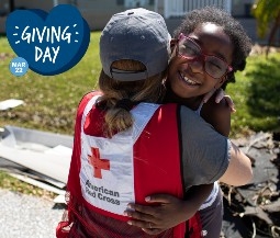red cross volunteer in branded vest hugs girl with glasses