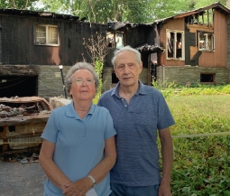 two people stand outside home destroyed by fire
