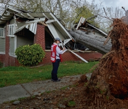 red cross volunteer stands outside home destroyed by storms