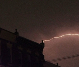 lightning appears near the corner of a building that is otherwise silhouette and in very low light