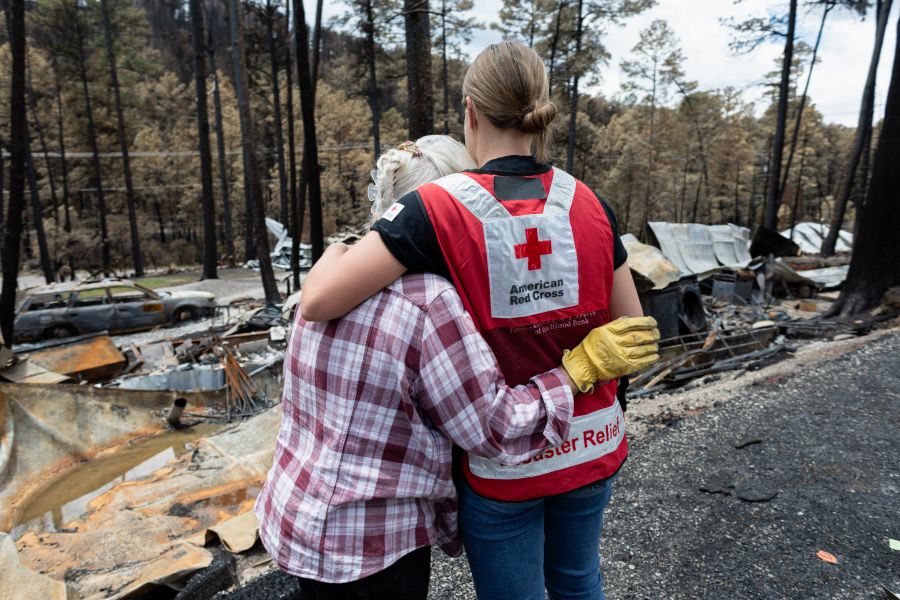 a Red Cross volunteer hugs woman impacted by a disaster as they overlook the damage