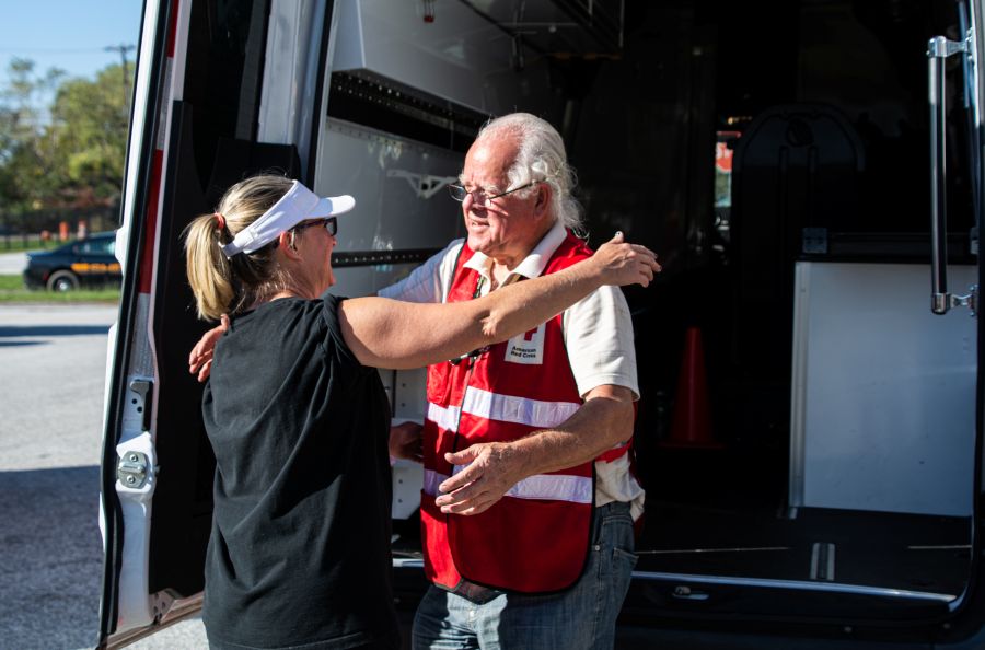 a male Red Cross volunteer hugs a woman in front of an emergency response vehicle