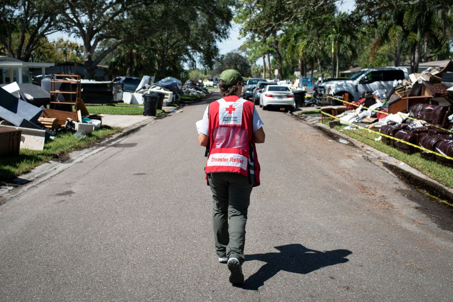 a Red Cross volunteer walks down a street surrounded by hurricane damage