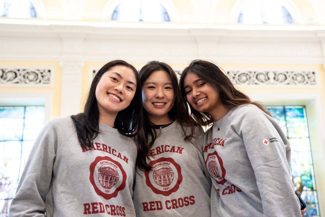 Three girls in Red Cross sweatshirts smile together
