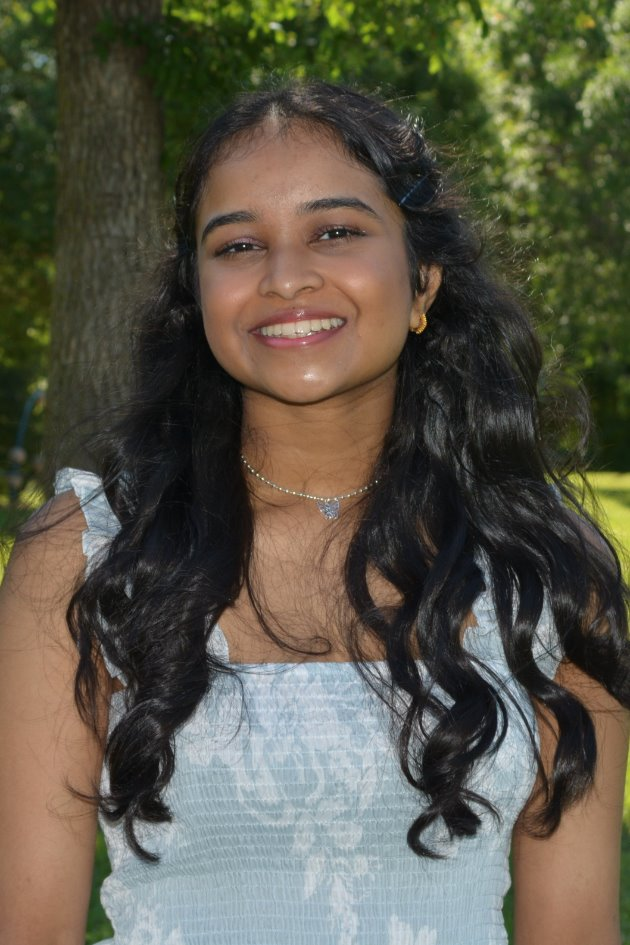 Isha Gandi, a young woman wearing a light blue and white summer dress, with dark brown hair. 