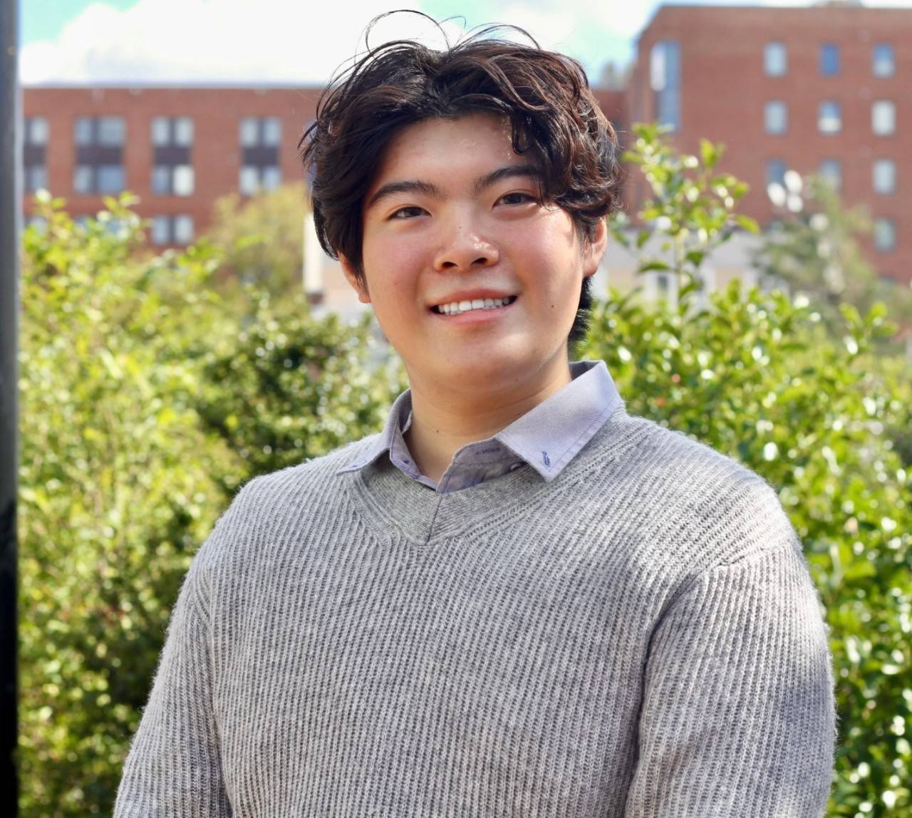 Jay Qiu, a young man wearing a gray sweater over a gray collared shirt, with short black hair. 
