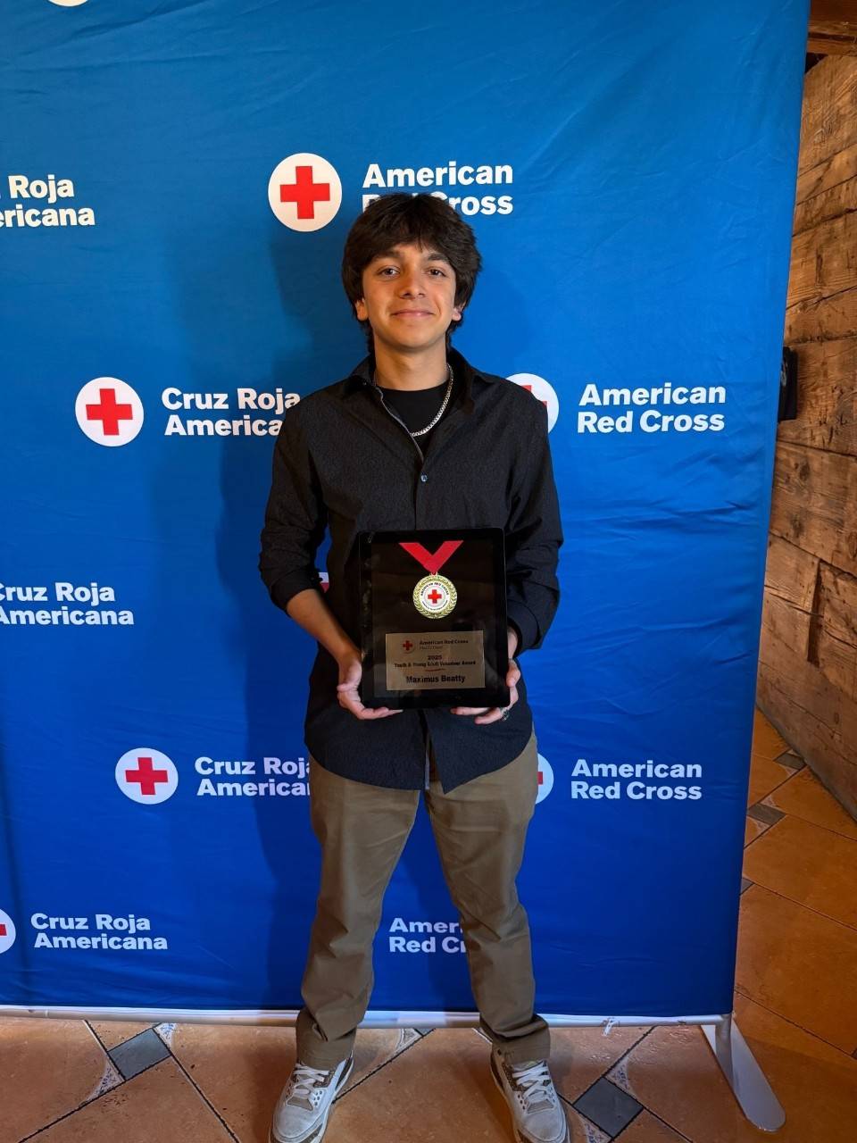 Maximus Beatty, a young man wearing adark blue button up shirt, with dark brown hair, holding an award. 
