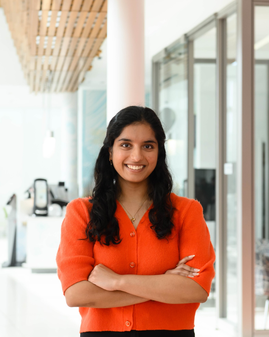 Tulsi Patel, a young woman wearing an orange blouse, with dark brown hair. 