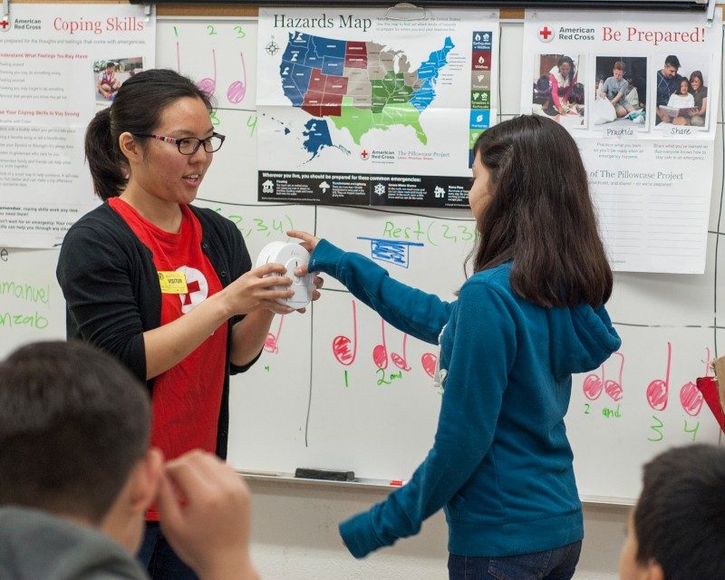 Red Cross volunteer teaching young girl how to use a smoke alarm