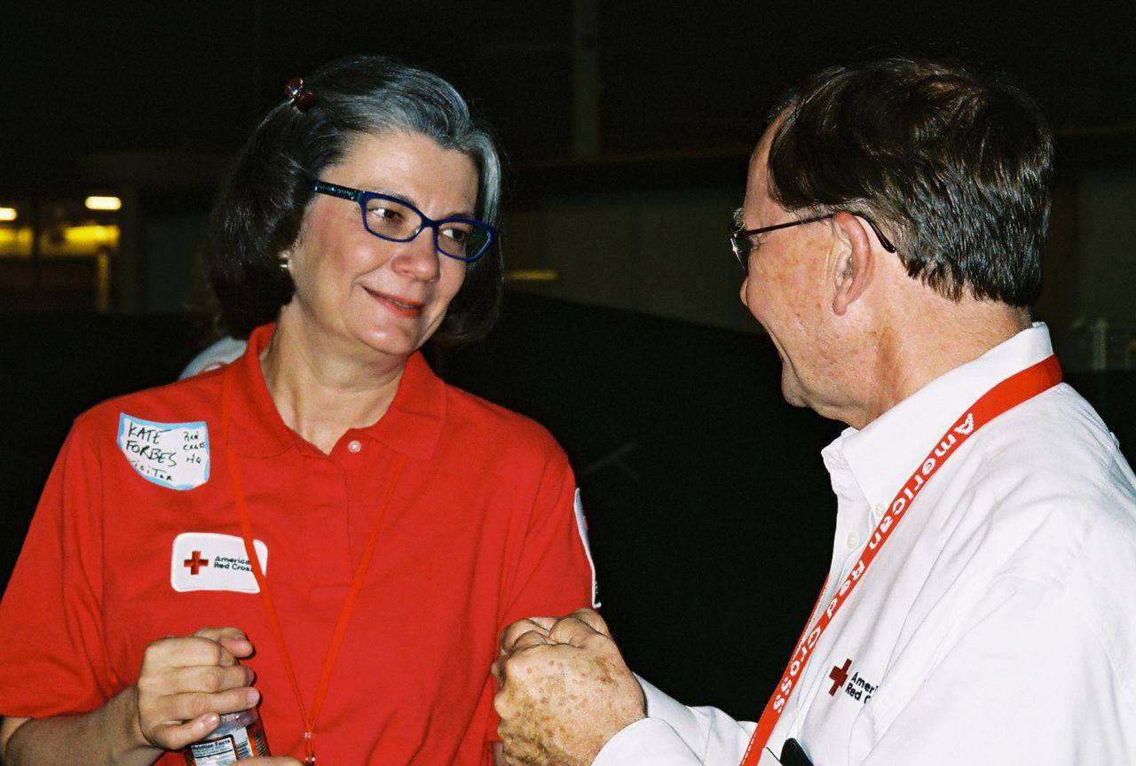 Kate Forbes in a red Red Cross polo speaking to another person wearing a white button down shirt. 