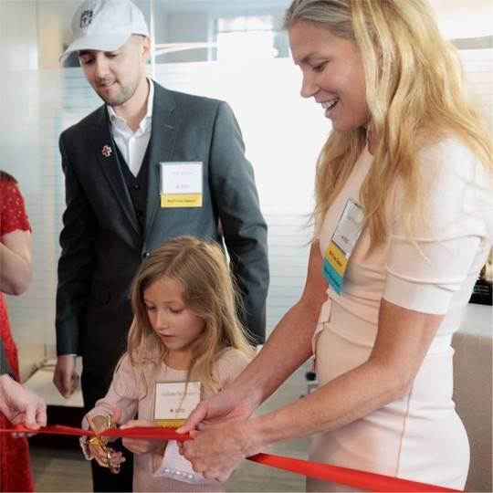 Leah Sylvester holding a red ribbon for a child to cut at a ceremony.