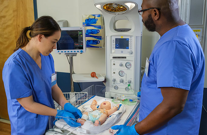 Neonatal resuscitation training with two healthcare professionals on infant manikin.
