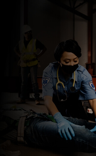 Two first responders treat an injured construction worker while three other workers look on.