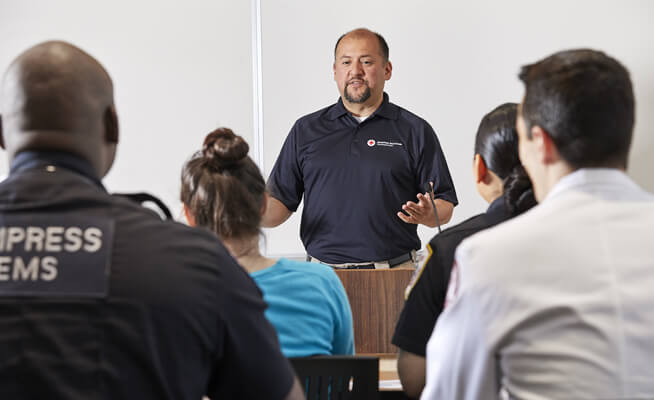 Image of an Instructor teaching a class to a group of individuals.