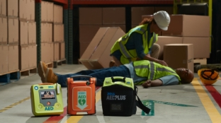 Image of a warehouse worker checking on the welfare of an incapacitated coworker with three AEDs on display.