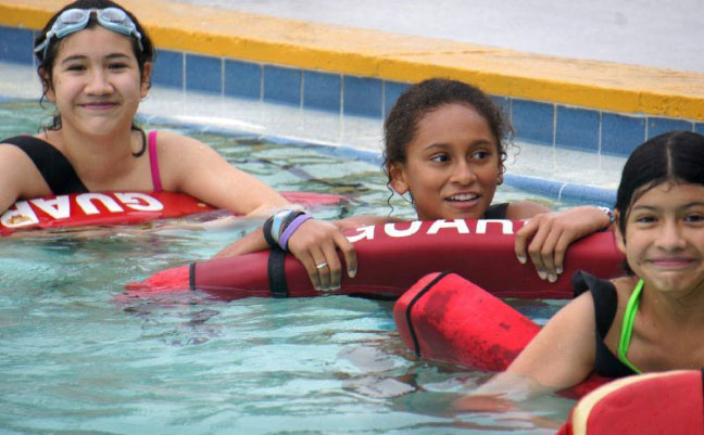 Image of three individuals holding lifeguard pool rescue tubes during a Red Cross Lifeguard training.