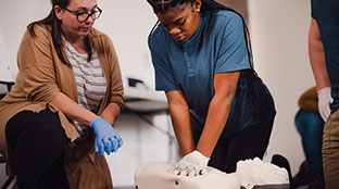 Instructor teaching student CPR/AED/First Aid while student demonstrating skills on a manikin.