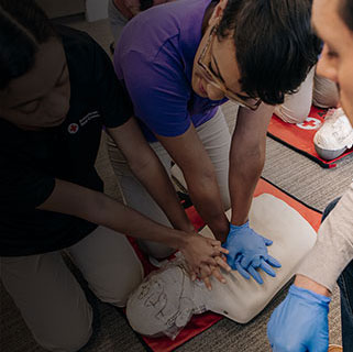 Students perform CPR compressions on a manikin while an instructor observes.