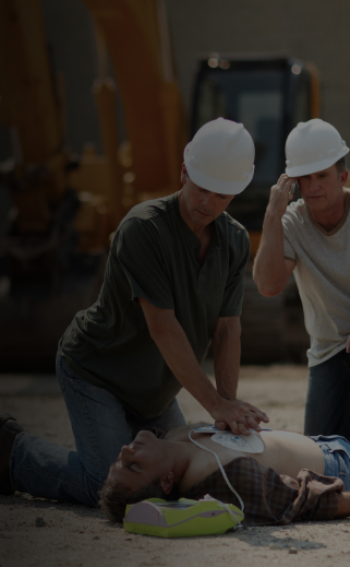 Image of 2 Construction workers using an AED and performing CPR on a coworker in distress on the worksite.