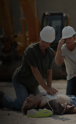 Image of 2 construction workers using an AED and performing CPR on a coworker in distress on the worksite.