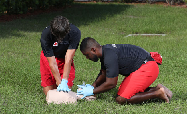 Image of two lifeguards performing CPR on a CPR manikin in the grass.