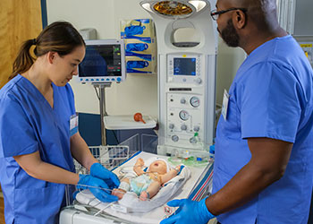 Neonatal resuscitation training with two EMS professionals on infant manikin.