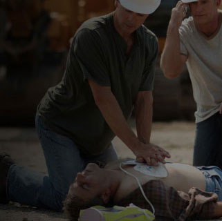 Two construction workers using an AED and performing CPR on a coworker in distress on the worksite.