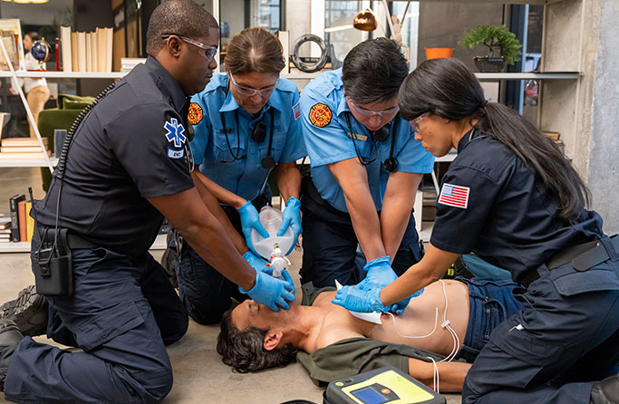 EMS team performing CPR and using an AED and bag valve mask on an unconscious person.
