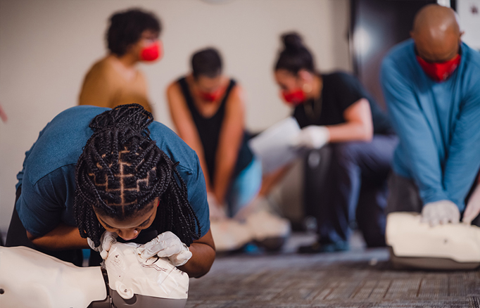 Individuals in a CPR training class practicing chest compressions and breaths on CPR manikins.