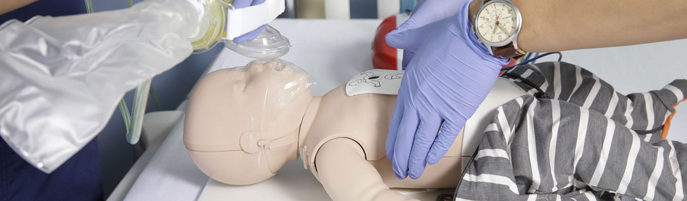 Two healthcare professionals in PALS course begin resuscitation on an infant using chest compressions and oxygen.