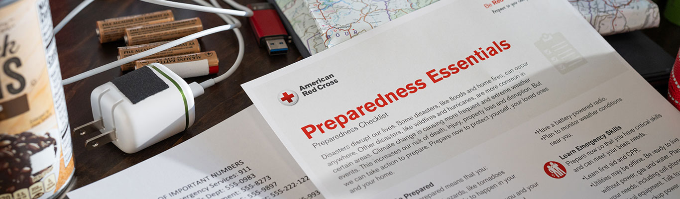 Red Cross Preparedness Essentials Checklist in front of basic supplies including batteries and a phone charger.