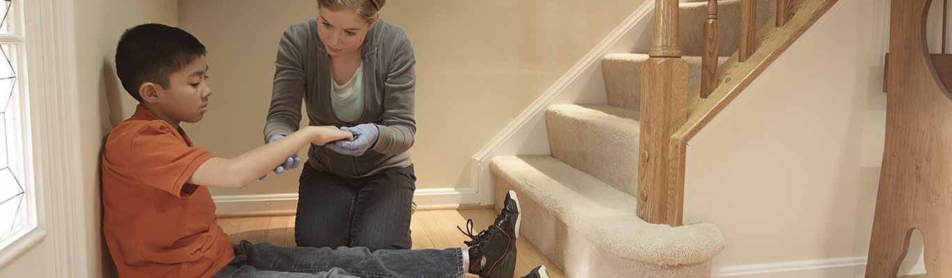 Age-appropriate babysitter providing first aid to child at the bottom of the stairs.