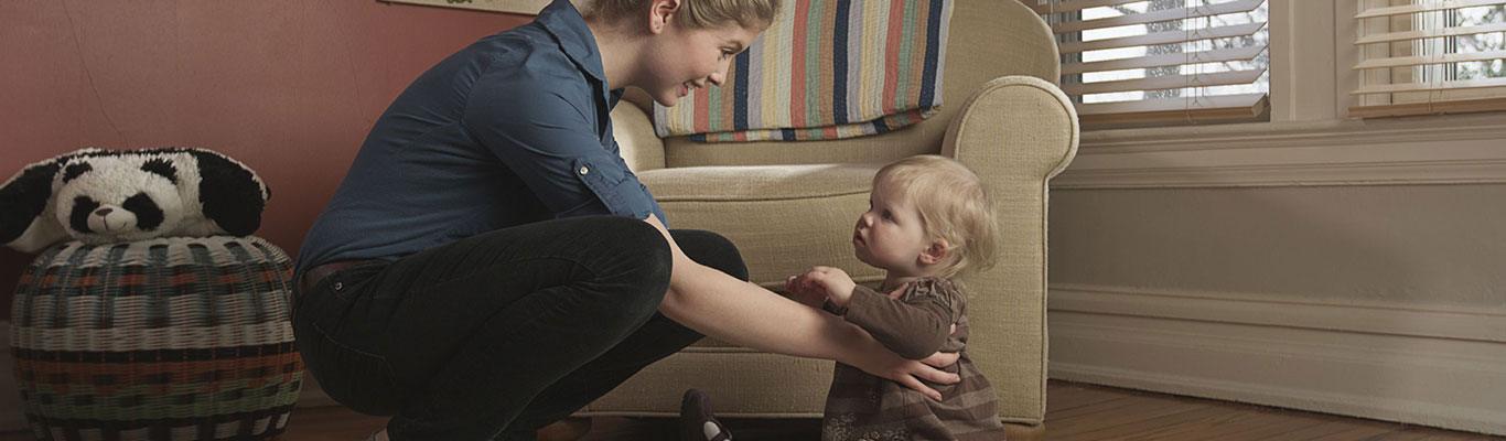 Nanny holding a toddler in a living room.
