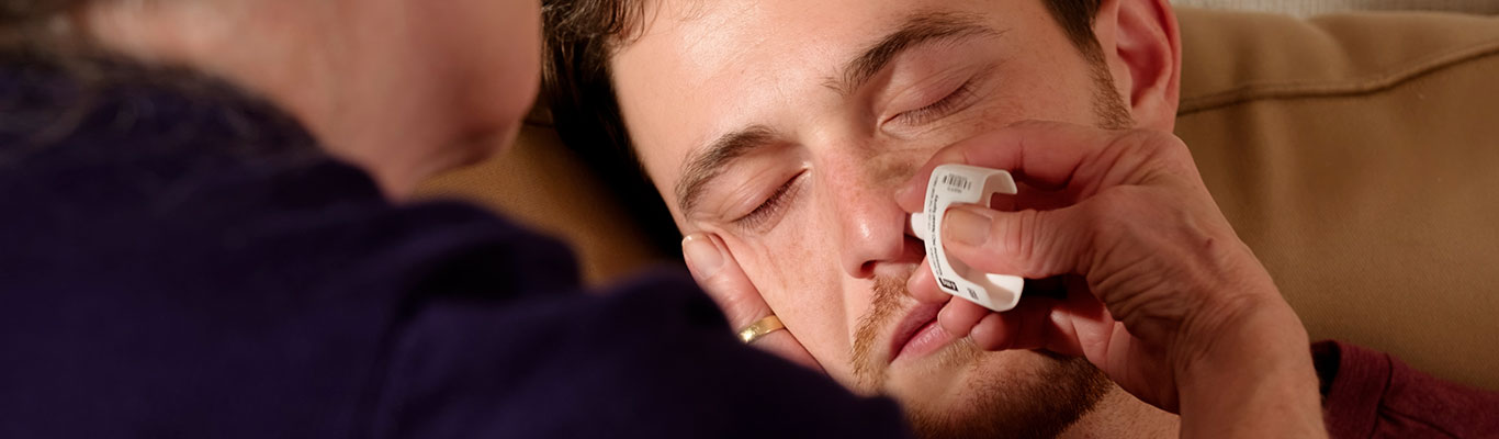 A person experiencing signs of opioid overdose while another person administers naloxone nasal spray.