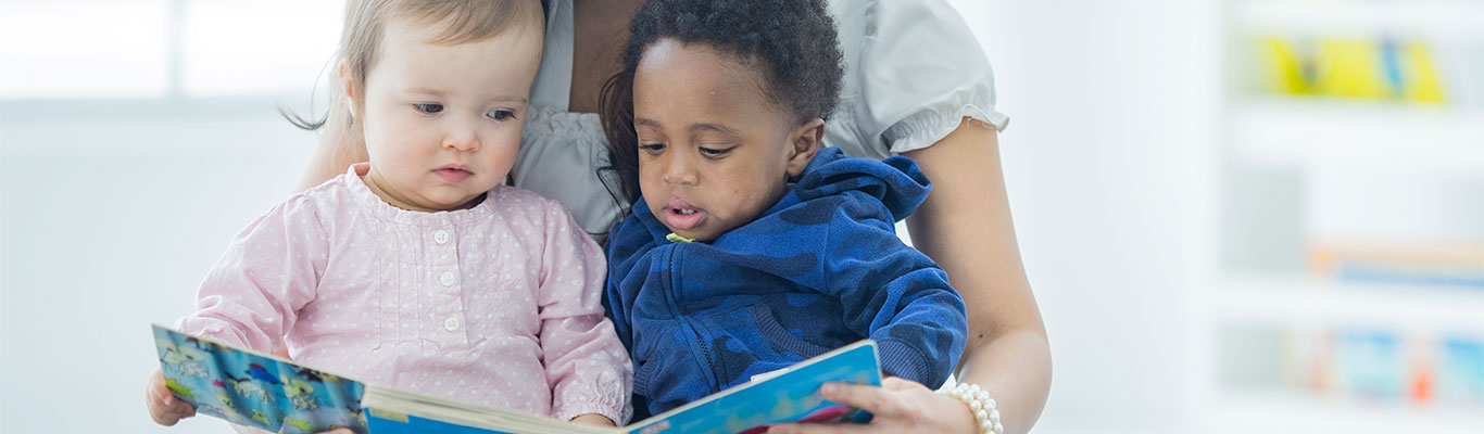 Babysitter reading a book to two children.