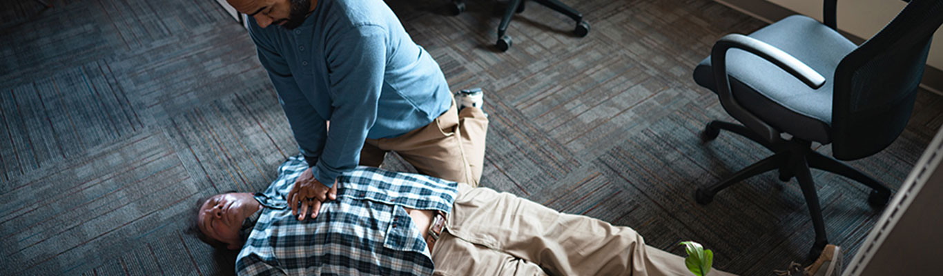 Bystander performing CPR on an unconscious person in an office setting, demonstrating chest compressions during a cardiac emergency.