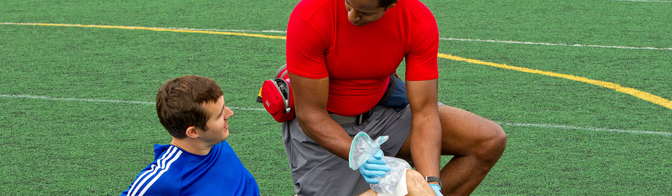 Personal trainer providing first aid to soccer player on field.