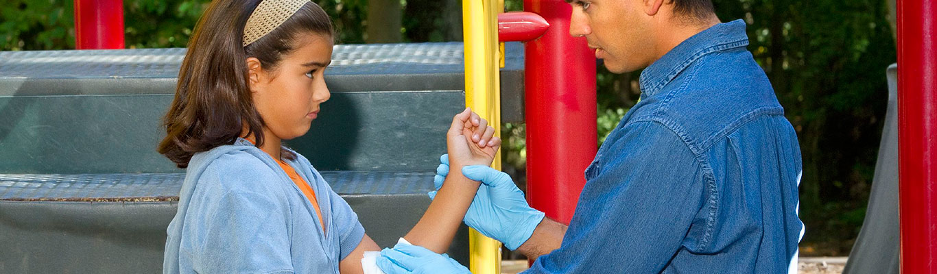 Parent performing first aid on child at a playground.