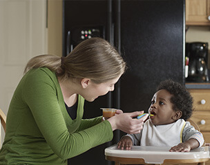 Young woman babysitter feeding a baby in a high chair.