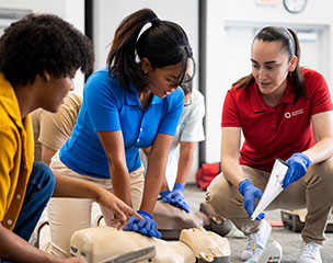 Red Cross Instructor teaching students techniques for CPR compressions with CPR manikins.