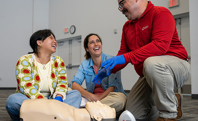 Red Cross Instructor teaching two students CPR with a CPR manikin and pocket mask.