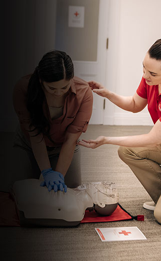 Red Cross instructor training a student on CPR with a manikin.
