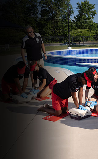Lifeguarding instructors teaching students CPR using Red Cross resuscitation equipment.