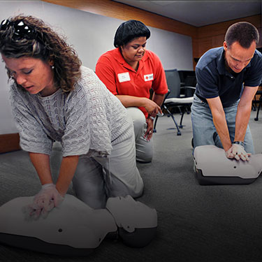 A group of students practicing compressions on CPR manikins with a Red Cross instructor.