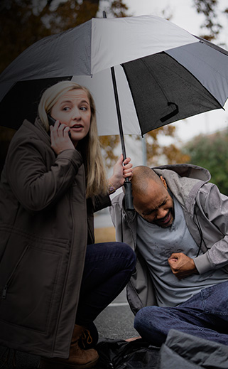 Woman being a lifesaver by calling 911 while man is on ground holding stomach.