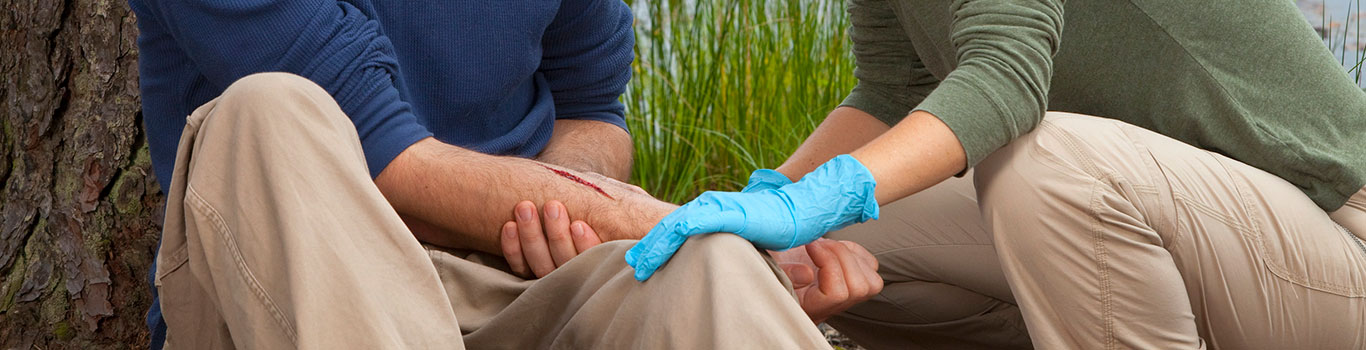 A person applying first aid to someone with a cut on their arm in the wilderness.